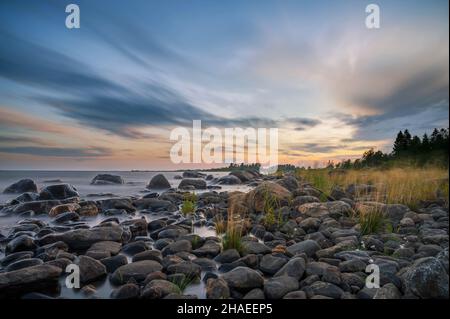 Lunga esposizione di un magnifico tramonto morbido e colorato vicino alla pietra del mare. Bel movimento nube con pietre di mare. Foto Stock