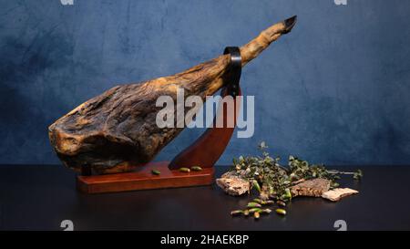 Prosciutto iberico spagnolo alimentato con ghiande, pata negra esposto in stativo di prosciutto di legno con fondo blu Foto Stock