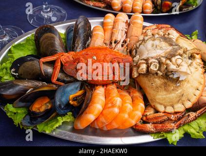 Piatto di pesce sulla tovaglia blu. Cozze, gamberetti, granchio marrone, granchio ragno e scampi Foto Stock