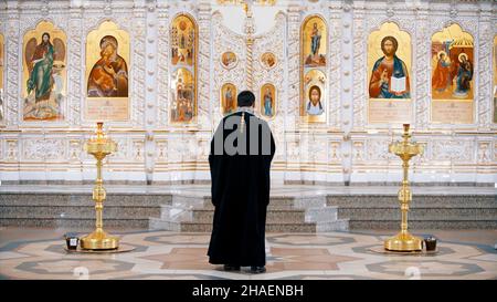 L'iconostasi all'interno di una chiesa ortodossa. Video. Vista posteriore di un prete che si trova di fronte alle icone con i volti dei santi, concetto di religi Foto Stock