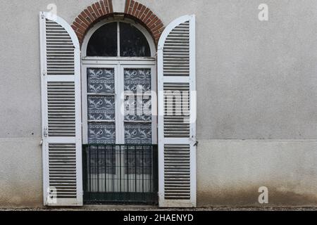 persiane piantagione dipinte di bianco si aprono e sono inchiodati contro un muro per rivelare una finestra di vetro con tende bianche a rete Foto Stock