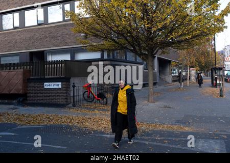 Donna che si mescola con le foglie gialle dell'autunno nella zona conosciuta come St Lukes il 23rd novembre 2021 a Londra, Regno Unito. St Lukes è un distretto nel centro di Londra, nel comune di Islington. Si trova appena a nord del confine con la città di Londra, vicino alla tenuta Barbican. Foto Stock