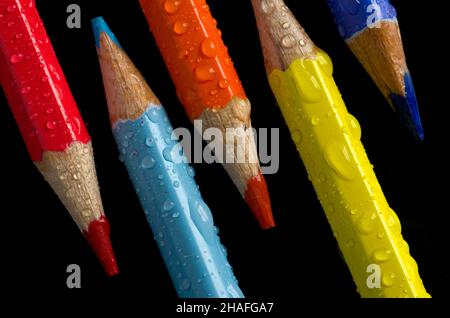 Immagine macro di Crayon rosso, arancione, blu e giallo con gocce d'acqua su nero verticale Foto Stock