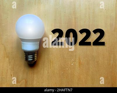 Festeggiamo il prossimo 2022 scritto in testo. Lampadina e sfondo in legno Foto Stock