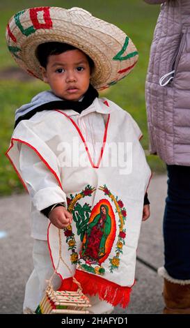 Wilkes barre, Stati Uniti. 12th Dic 2021. Un ragazzo vestito con abiti messicani tradizionali guarda la processione durante una festa della Guadalupa. La Madonna di Guadalupe viene celebrata ogni 12 dicembre perché si crede che Guadalupe si sia mostrata a Juan Diego in Messico. Localmente una statua di Guadalupe trascorre un anno in una casa di famiglia, il giorno di festa c'è una processione dalla casa alla chiesa dove si tiene una messa. Credit: SOPA Images Limited/Alamy Live News Foto Stock