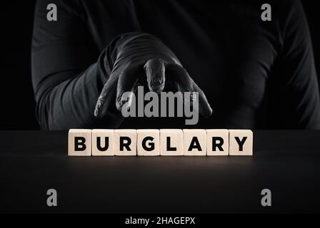 Furto, crimine, furto o furto. Ladro mano con guanti neri sopra la parola burglary scritto su blocchi di legno. Foto Stock