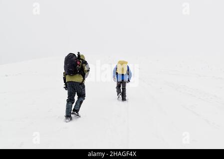 Escursionisti che saliscono in montagna in neve profonda e cattive condizioni meteorologiche