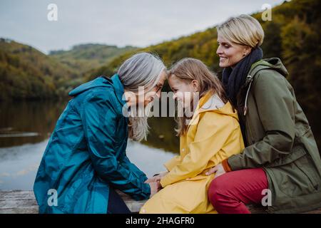 Bambina con madre e nonna seduta su panca e divertirsi outoors vicino al lago. Foto Stock