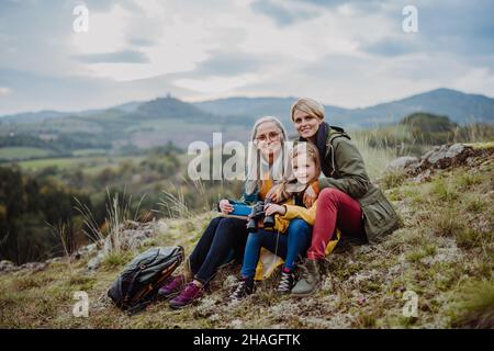Bambina con madre e nonna seduta e lookiong alla macchina fotografica sulla cima della montagna. Foto Stock