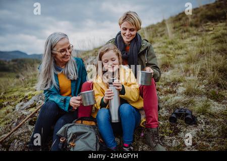 Bambina con madre e nonna seduta e bere tè caldo in cima alla montagna. Foto Stock