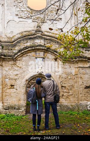 Uomo dai capelli grigi e giovane ragazza snella dai lunghi capelli biondi esamina le rovine dell'antica sinagoga. Viaggiatore con zaino. Moldavia. Rashkov. Selez Foto Stock