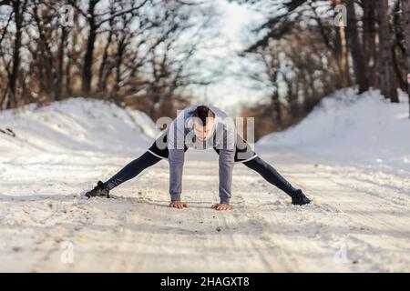 Sportivo in forma in piedi su sentiero nevoso in natura e fare esercizi di riscaldamento e stretching. Fitness invernale, flessibilità, vita sana Foto Stock