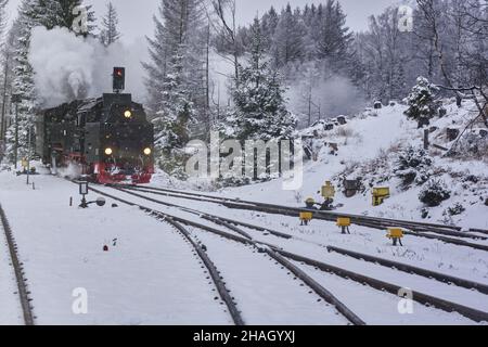 Locomotiva a vapore con camino fumante e fumante si sta dirigendo verso i commutatori innevati delle piste nella foresta in inverno Foto Stock