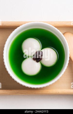 Vista dall'alto del matcha grande tangyuan (tang yuan) con zuppa di matcha dolce e pasta di fagioli rossi in una ciotola su sfondo bianco tavolo per cibo festival. Foto Stock