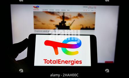 Persona che detiene il cellulare con il logo della società francese di petrolio e gas TotalEnergies se sullo schermo di fronte al sito web aziendale. Mettere a fuoco sul display del telefono. Foto Stock