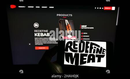 Persona che tiene il cellpohone con il logo della compagnia israeliana di carne coltivata ridefinire Meat Ltd. Sullo schermo di fronte al sito web. Mettere a fuoco sul display del telefono. Foto Stock