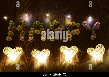 Su uno sfondo di legno, la parola FELICE è scritto in grandi lettere di fiori multicolore. I cuori incandescenti sono disposti in una linea dal basso Foto Stock