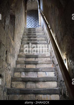 Una ripida scalinata di pietra molto antica tra due pareti di pietra che porta ad una porta di legno chiodata. Un corrimano corre la lunghezza delle scale. Foto Stock