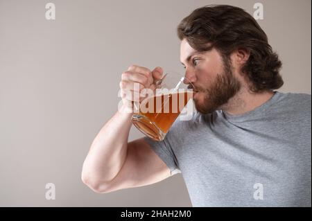 uomo che beve birra con una tazza grande su uno sfondo grigio Foto Stock