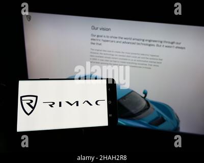 Persona che tiene smartphone con logo del produttore di auto croato Rimac automobili sullo schermo di fronte al sito web. Mettere a fuoco sul display del telefono. Foto Stock