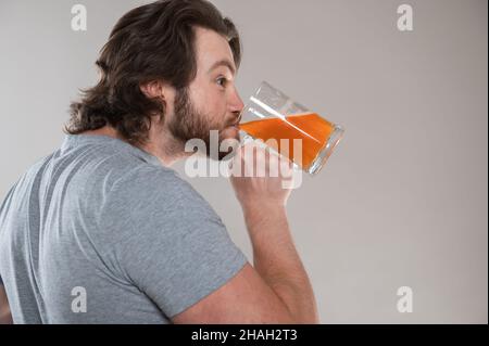 divertente uomo bearded bere birra con una tazza grande su uno sfondo grigio Foto Stock