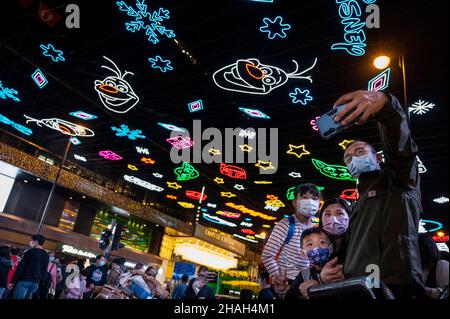 Hong Kong, Cina. 11th Dic 2021. HONG KONG, CINA - 11 DICEMBRE: Una famiglia prende un selfie con luci di Natale che coprono una strada a Hong Kong il 11 dicembre 2021. Hong Kong è in forte allerta la diffusione della variante Omicron durante le vacanze. (Foto di Miguel candela/SOPA Images/Sipa USA) Credit: Sipa USA/Alamy Live News Foto Stock