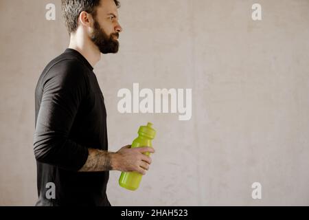 Uomo bianco bearded di mezza età che tiene bottiglia d'acqua che cammina all'interno Foto Stock
