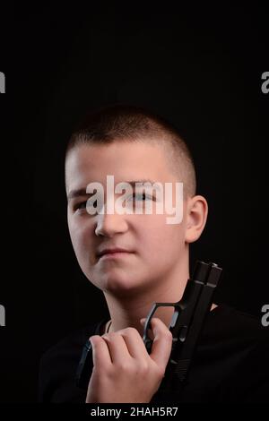 Giovane ragazzo con una pistola con un taglio corto su sfondo molto scuro. Guarda direttamente nella fotocamera Foto Stock