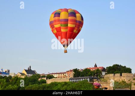 Una grande mongolfiera multicolore vola a bassa velocità su edifici antichi e una valle densamente boscosa. Fotografato a distanza ravvicinata Foto Stock