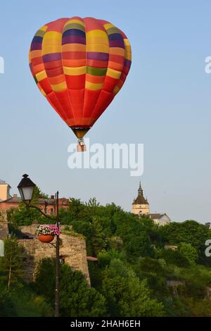 Una grande mongolfiera multicolore vola a bassa velocità su edifici antichi e una valle densamente boscosa. Fotografato a distanza ravvicinata Foto Stock