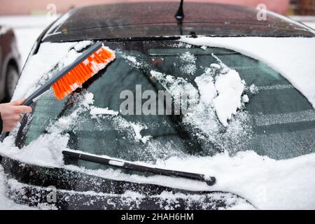 Problemi invernali con la vettura. Un uomo pulisce l'auto dalla neve con una spazzola Foto Stock