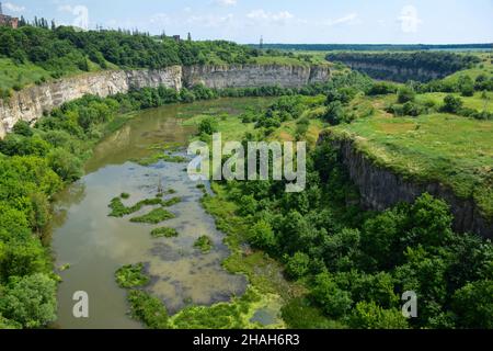 Vista del fiume precedente che è diventato una palude. I lati sono cresciuti di alberi. Scogliere rocciose sui lati Foto Stock