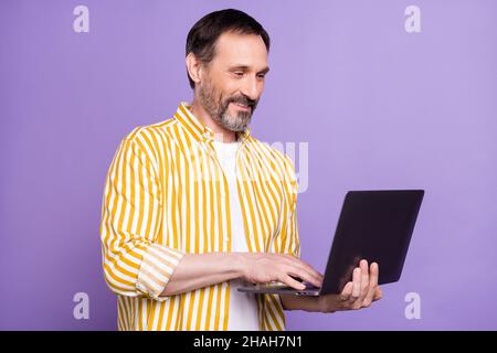 Ritratto di foto barbato uomo in maglia a righe sorridente utilizzando il computer portatile lavoro isolato pastello viola sfondo di colore Foto Stock