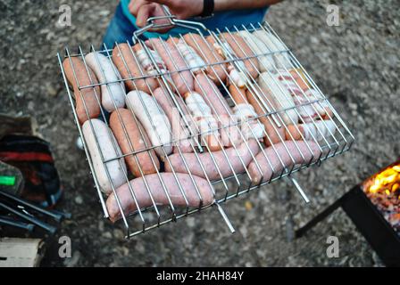 Diversi tipi e colori di salsicce con carne vengono fritti su un fuoco nella foresta Foto Stock