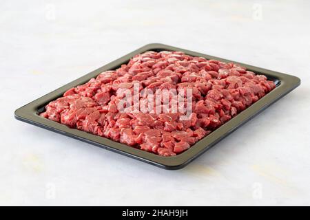 Cubetti di carne di vitello crudo tritati da saltare su tavola di legno bianco. Foto Stock