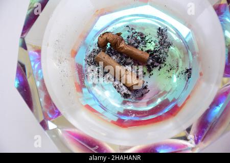 Due sigari affumicati si trovano sulle ceneri in un posacenere sfaccettato di cristallo da vicino Foto Stock