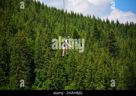 La ragazza saltò dal bungee jumping ride, si appende su una corda stretta ad un'alta quota e sorride. Su uno sfondo sfocato di una montagna Foto Stock