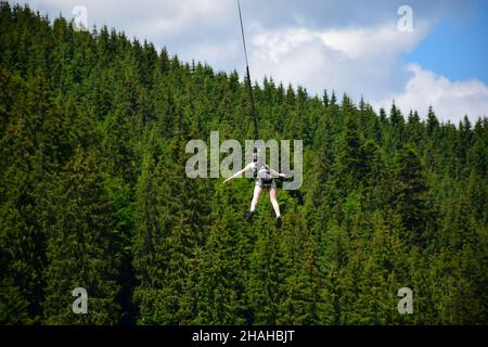 La ragazza saltò dal bungee saltando, si appende su una corda stretta ad un'altitudine elevata. Su uno sfondo sfocato di una montagna Foto Stock