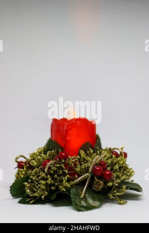 Candela rossa con fiamma, candela rossa con corona verde e bacche rosse su sfondo bianco, decorazione natalizia, decorazione a candela, biglietto di Capodanno, Foto Stock