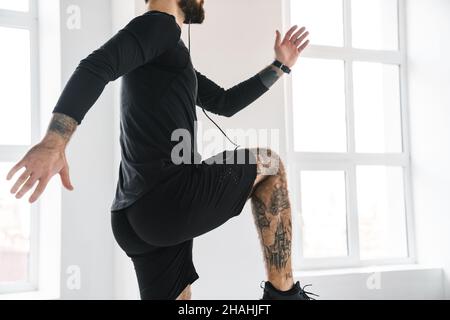 Giovane bruna ported uomo bianco in abbigliamento sportivo che si esercita saltando in interni ascoltando la musica in cuffie vista laterale ritagliata Foto Stock