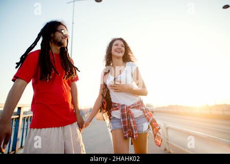 Coppia multirazziale che cammina lungo la strada sorridendo. Ritorno dal festival musicale di mattina presto. Foto Stock