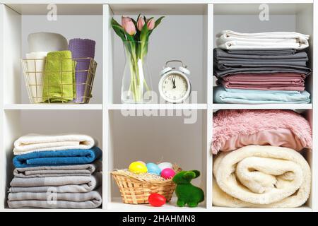 Organizzazione dello storage. Pile di asciugamani, lenzuola, lenzuola, coperte e cuscini su una mensola bianca. Festa di Pasqua Foto Stock