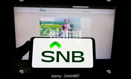 Persona che tiene uno smartphone con il logo della società finanziaria Saudi National Bank (BNS) sullo schermo di fronte al sito Web. Mettere a fuoco sul display del telefono. Foto Stock