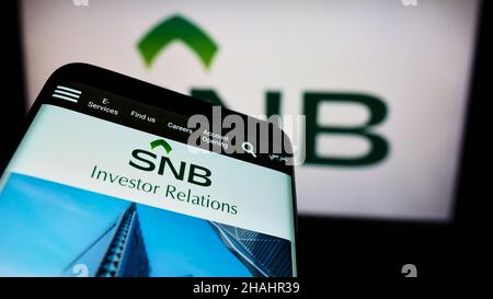 Telefono cellulare con logo della società finanziaria Saudi National Bank (BNS) sullo schermo di fronte alla pagina web aziendale. Mettere a fuoco sul display del telefono. Foto Stock