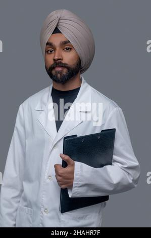 Tranquillo medico indiano in un camice da laboratorio guardando avanti Foto Stock