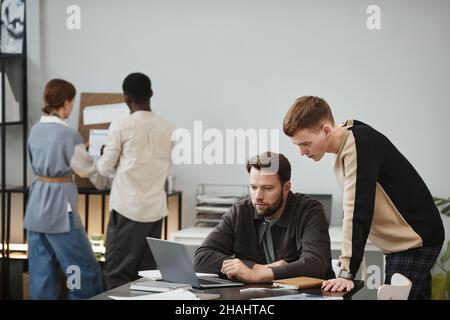 Designer seduto sul posto di lavoro e lavorando su un notebook, ha discusso qualcosa con il suo collega in ufficio Foto Stock
