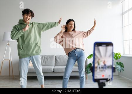 Giovane coppia asiatica che registra contenuti video, ballando con la fotocamera dello smartphone a casa. Concetto di vlogging Foto Stock