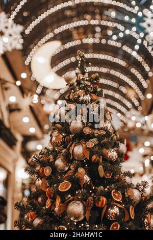 Interessante albero di Natale creativo decorato con arance secche, mandarini, coni di pino e palle di Natale dorate. Dettagli magici. Stagione invernale in ho Foto Stock