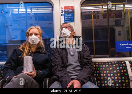 LONDRA, REGNO UNITO. 13 dicembre 2021. Due viaggiatori sulla metropolitana di Londra indossando maschere protettive dopo che il primo ministro Boris Johnson ha annunciato un'emergenza omicron in un discorso televisivo da Downing Street la Domenica sera e un programma di richiamo con jab covid da offrire a tutti gli oltre 18 in Inghilterra da questa settimana per combattere il rapida diffusione della variante omicron. Credit: amer Ghazzal/Alamy Live News Foto Stock