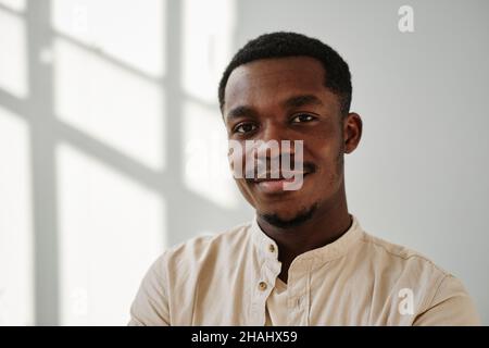 Ritratto del giovane africano in camicia casual sorridendo a macchina fotografica contro la parete bianca Foto Stock